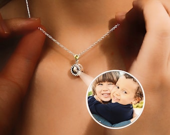 May include: A silver necklace with a small round pendant featuring a photo of two children. The pendant has a small yellow gemstone accent.