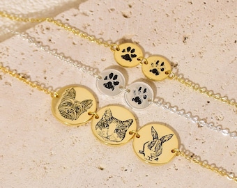 May include: Three gold necklaces with round charms. The top necklace has two paw print charms. The middle necklace has a paw print charm, a cat charm, and a dog charm. The bottom necklace has a rabbit charm, a cat charm, and a dog charm.