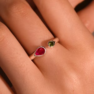 Peut inclure: Bague ouverte avec une pierre rouge en forme de goutte et une petite pierre verte ronde. La bague est en métal doré. Les pierres sont serties dans un métal argenté.