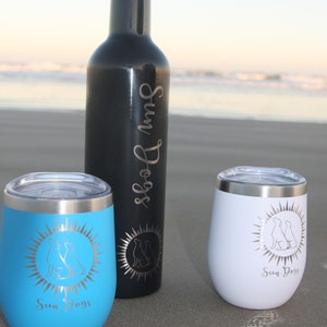 Puede incluir: Dos vasos de acero inoxidable con un dise&ntilde;o de sol y dos perros, uno azul y otro blanco, y una botella de acero inoxidable negra con el texto "Sun Dogs" en ella.