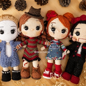 K&ouml;nnte beinhalten: Vier geh&auml;kelte Puppen, die als Horrorfilmfiguren verkleidet sind. Die Puppen stehen auf einer Holzoberfl&auml;che. Die Puppen tragen rote, blaue, schwarze und braune Kleidung. Die Puppen haben schwarze Augen und rote Lippen. Die Puppen halten Requisiten aus den Filmen, als die sie verkleidet sind. Die Puppen l&auml;cheln alle.