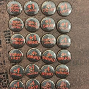 Può includere: Una collezione di ventiquattro gettoni di gioco neri e rossi. Ogni gettone ha un numero uno rosso e una parola o frase in rosso, come "Danno", "Per colpire" e "Salva". I gettoni sono disposti su una superficie marrone.