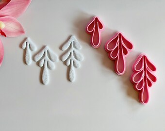 May include: An overhead shot displays six leaf-shaped objects. Three are white, textured, and solid. The other three are pink, plastic cookie cutters. A pink orchid flower is in the upper left corner. The objects are arranged on a white surface.