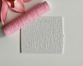 May include: A pink textured rolling pin and a white textured square are displayed on a white surface. The rolling pin has a crosshatch pattern. A pink orchid flower is in the upper left corner.