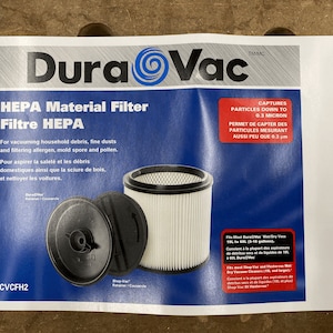 May include: White HEPA filter for vacuum cleaners. The filter is cylindrical with a black top and bottom. The filter is labeled "DuraVac" and "CVCFH2". The text on the packaging says "captures particles down to 0.3 micron".