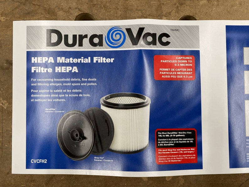 May include: White HEPA filter for vacuum cleaners. The filter is cylindrical with a black top and bottom. The filter is labeled "DuraVac" and "CVCFH2". The text on the packaging says "captures particles down to 0.3 micron".