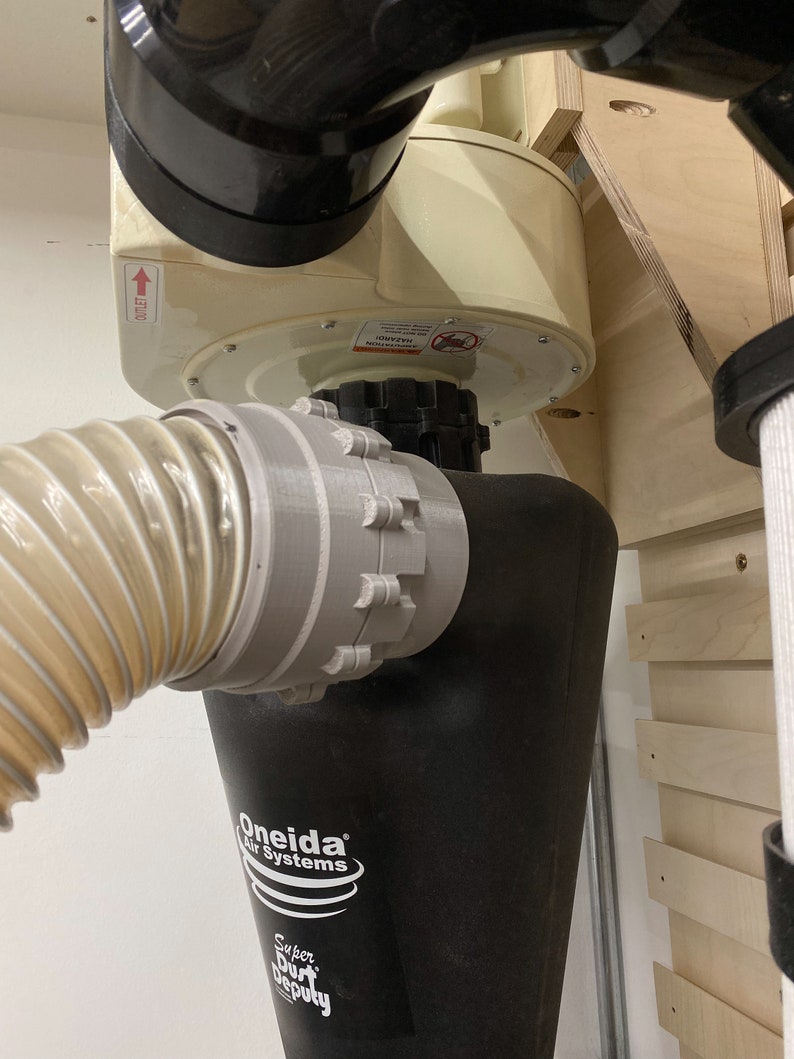 May include: A black dust collection system with a white Oneida Air Systems logo and the text "Super Dust Deputy". The system is mounted to a wall and has a clear hose attached to it.