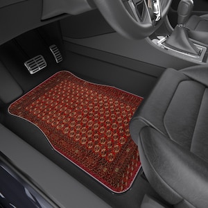 May include: A red and brown patterned car floor mat with a white border. The mat is placed in the driver's side footwell of a car, near the pedals and seat. The pattern resembles a traditional rug design.
