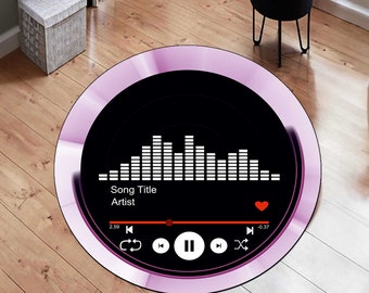 May include: A round pink and black rug with a music player graphic. The graphic shows a song title, artist, and a progress bar with play and pause buttons. The text on the graphic reads "Song Title" and "Artist".