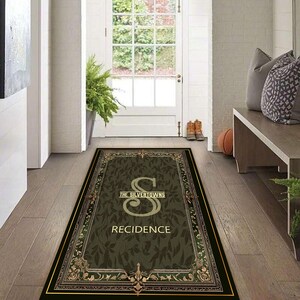 Può includere: Un zerbino rettangolare con sfondo verde scuro e bordo decorativo. Il tappeto presenta il testo "THE SILVERTOWNS" sopra una grande lettera "S" e la parola "RECIDENCE" sotto. Il design include elementi floreali e ornamentali.