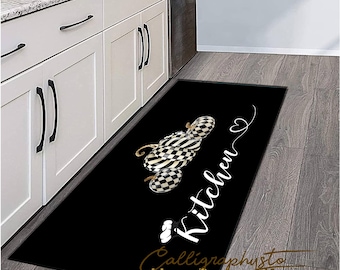 May include: Black and white checkered pumpkin design kitchen rug with the text "Kitchen" in white cursive lettering. The rug has a black border and the text "Calligraphysto ideas-Design-Life" in gold lettering.