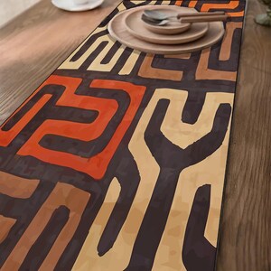 May include: A rectangular table runner with a geometric pattern in shades of brown, orange, and beige. The runner is placed on a wooden table, with wooden plates and silverware visible on top.