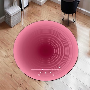 May include: Pink round rug with a concentric circle design. The rug has a music player icon with play, pause, and skip buttons.