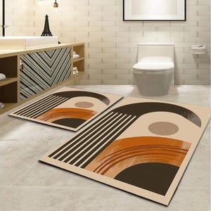 Puede incluir: Dos alfombrillas rectangulares con fondo beige y un diseño gráfico de líneas paralelas negras, un arco grande de color marrón oscuro, un círculo beige sólido y un semicírculo naranja texturizado con detalles de pinceladas.