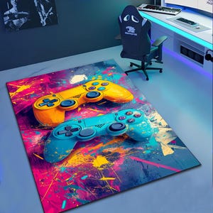 Puede incluir: Una alfombra colorida con un diseño de mando de videojuego azul y amarillo. La alfombra tiene un diseño abstracto de salpicaduras de pintura azul, rosa, amarillo y blanco.