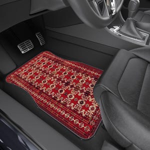 May include: A red and beige patterned car floor mat with an oriental rug design. The mat is rectangular with a curved edge to fit the car's interior. The mat is placed in the driver's side footwell.