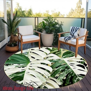 May include: A round rug with a white and green tropical leaf pattern. The rug is on a wooden floor with two white chairs and potted plants.