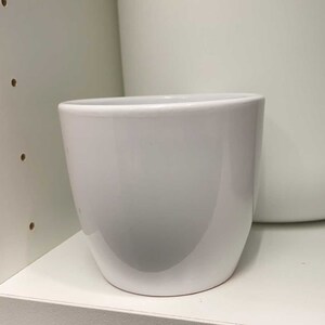 May include: A white ceramic planter with a rounded bottom and a smooth, glossy finish.
