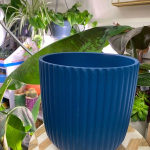 May include: A dark blue planter with vertical ridges. The planter is made of a smooth, matt material and has a rounded bottom.