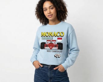 May include: Light blue sweatshirt with a graphic of a red and white race car, the word "MONACO" in yellow, and the text "WORLD CHAMPIONSHIP 1988". The sweatshirt is a crew neck style.