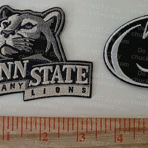 May include: Two embroidered patches featuring Penn State University logos. One patch shows a cougar head above "PENN STATE NITTANY LIONS." The other is an oval with a white "P" logo on a black background. A ruler is at the bottom.
