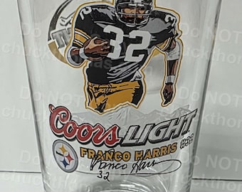 Puede incluir: Vaso transparente con un jugador de fútbol americano con uniforme negro y dorado, número 32. El vaso muestra el logotipo de Coors Light y el nombre "Franco Harris".