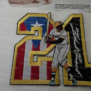 May include: Embroidered patch featuring a baseball player in a Pirates uniform, holding a bat. The number "21" is prominently displayed, with the Puerto Rican flag incorporated into the design. The player's signature is also visible.