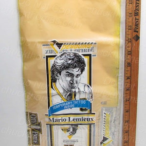 May include: A yellow plastic bag with a yellow and black City Pride bread label. The bag contains a temporary tattoo of Mario Lemieux, a Pittsburgh Penguins hockey player. The bag also includes a Pittsburgh Penguins sticker.