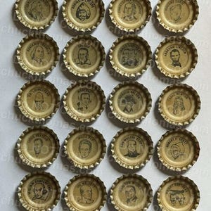May include: A collection of twenty-one vintage bottle caps, each featuring a portrait of a historical figure. The caps are metallic gold with black and white illustrations. Notable figures include Marie Curie, Abraham Lincoln, and William Shakespeare. The caps are arranged in a grid.
