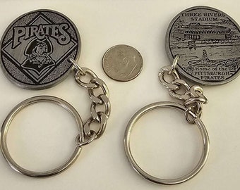 Peut inclure: Un porte-clés argenté avec deux breloques rondes en métal. Un charme présente une image en noir et blanc d'un pirate avec le mot "PIRATES" au-dessus. L'autre charme présente une image en noir et blanc d'un stade avec le texte "THREE RIVERS STADIUM" et "Home of the PITTSBURGH PIRATES".