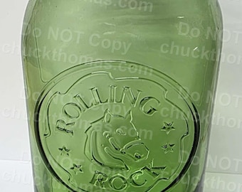May include: Green glass jar with a rounded base and a wide mouth. The jar features an embossed circular design with the words "Rolling Rock" and a horse. The jar is marked "Since 1939".