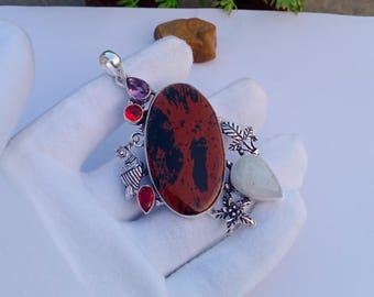 May include: A silver pendant with an oval, dark red and black stone as the centerpiece. The pendant is adorned with smaller red and purple stones, and a white teardrop-shaped stone. The design includes floral and leaf accents.