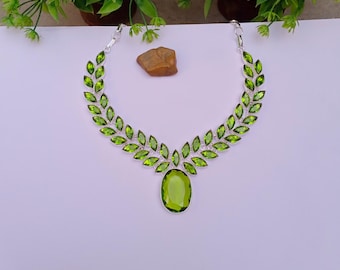 Könnte beinhalten: Eine silberne Halskette mit blattartigem Design, mit leuchtend grünen Edelsteinen. Die Halskette hat einen großen, oval geformten grünen Steinanhänger. Die Edelsteine sind in einem silbernen Metall gefasst.