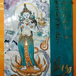 Pode incluir: Um azulejo de cerâmica colorido com uma pintura de uma divindade em pé sobre uma flor de lótus. A divindade está vestindo uma túnica azul e dourada e tem uma auréola ao redor de sua cabeça. O azulejo também apresenta um mantra sânscrito escrito em letras douradas.