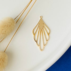 Könnte beinhalten: Goldfarbener Metallanhänger mit einem fächerförmigen Design. Der Anhänger hat ein zartes, filigranes Ausschnittmuster.