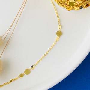 May include: A gold chain necklace with small round gold charms. The necklace is on a white surface.