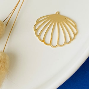 May include: Gold metal seashell charm with a cutout design. The charm has a hole at the top for attaching to jewellery or other crafts.