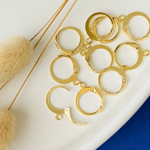 Peut inclure: Gros plan sur un groupe de crochets de boucles d'oreilles dorés. Les crochets sont disposés sur une surface blanche.