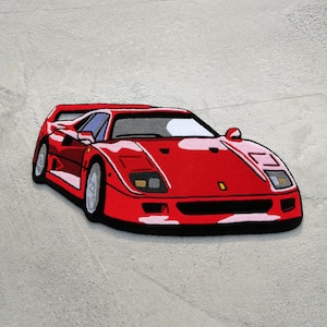 Könnte beinhalten: Ein roter Ferrari F40 Sportwagen-Teppich. Der Teppich ist aus weichem, plüschigem Material gefertigt und zeigt ein detailliertes Design des legendären Autos.