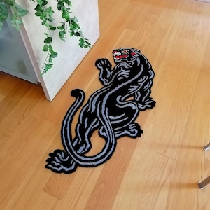 May include: Black and white rug with a stylized image of a panther. The rug is on a wooden floor.