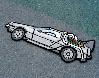 Könnte beinhalten: Ein grauer und schwarzer Teppich, der eine DeLorean-Zeitmaschine aus dem Film Zurück in die Zukunft darstellt. Der Teppich ist aus weichem, plüschigem Material gefertigt und zeigt ein detailliertes Design des kultigen Autos.