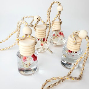 May include: Four glass bottles with dried flowers inside, each with a wooden cap and a beige string with gold accents. The bottles are hanging from the string.