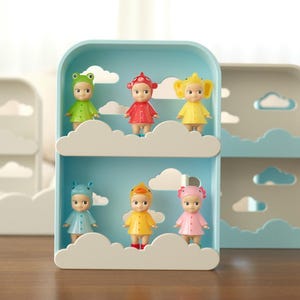 K&ouml;nnte beinhalten: Ein dekoratives Regal mit Wolkenmotiv, das kleine Puppen pr&auml;sentiert. Die Regale sind hellblau und wei&szlig;, mit wolkenf&ouml;rmigen Ausschnitten. Die Puppen sind in verschiedenen Farben gehalten, darunter Gr&uuml;n, Rot, Gelb und Rosa. Auf einem dunkelbraunen Tisch.