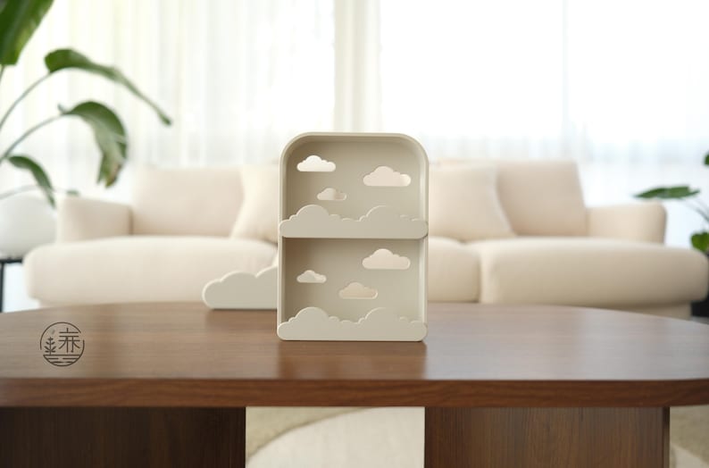 K&ouml;nnte beinhalten: Beige wolkenf&ouml;rmiges Regal mit zwei Ebenen und Wolkenausschnitten. Ein passendes wolkenf&ouml;rmiges Akzentst&uuml;ck befindet sich links. Das Regal steht auf einem dunkelbraunen Holztisch vor einem cremefarbenen Sofa.