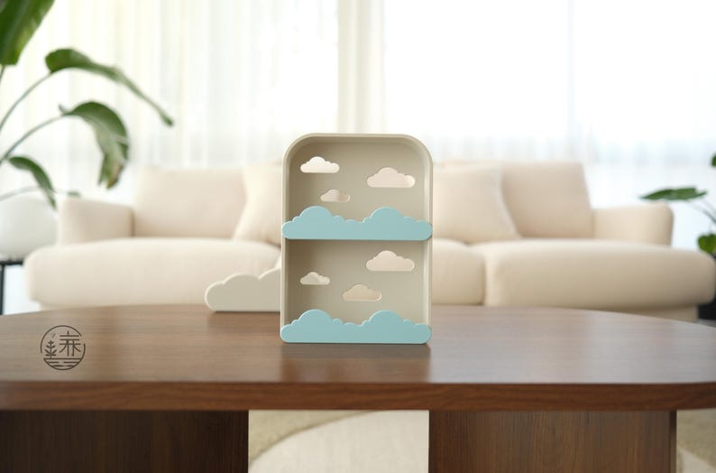 K&ouml;nnte beinhalten: Beige Regal mit Wolkenmotiv mit zwei Ebenen und Wolkenausschnitten. Das Regal hat hellblaue Wolkenakzente und wei&szlig;e Wolkenausschnitte. Es steht auf einem dunkelbraunen Holztisch. Eine wolkenf&ouml;rmige Dekoration.