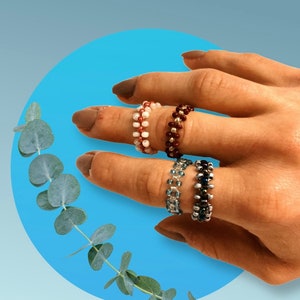 Könnte beinhalten: Drei Perlenringe an einer Hand. Die Ringe bestehen aus kleinen, bunten Perlen. Die Ringe sind auf dem Mittelfinger übereinander gelegt.