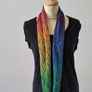 Könnte beinhalten: Ein mehrfarbiger Loop-Schal auf einer Schaufensterpuppe. Der Schal verläuft von Rot über Orange, Gelb, Grün bis Blau. Er hat ein zartes Lochmuster und besteht aus einem weichen, gestrickten Material. Dieser Schal ist ein Modeaccessoire.