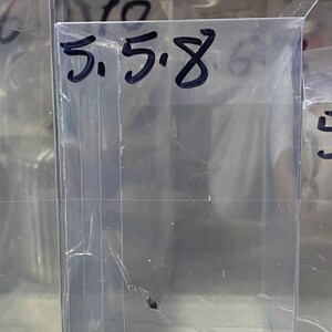 Peut inclure: Une boîte en plastique transparente avec une étiquette noire indiquant "5.5.8". La boîte est vide et semble être destinée au stockage.