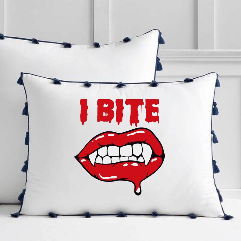 K&ouml;nnte beinhalten: Wei&szlig;es Kissen mit blauem Besatz und Quasten. Das Kissen zeigt eine rote und wei&szlig;e Grafik eines Vampirmundes mit Z&auml;hnen und dem Text "I Bite".
