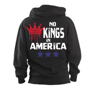May include: Black hooded sweatshirt with the text "NO KINGS IN AMERICA" in white block letters. A red crown graphic with dripping blood effect is above the text. Three blue stars are below the text.